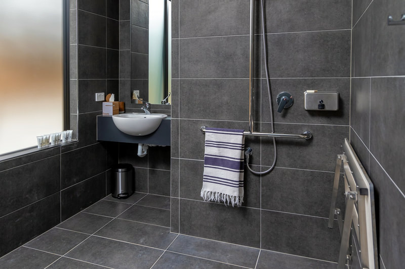 A beautiful floor to ceiling stone lined bathroom that is also disability compliant
